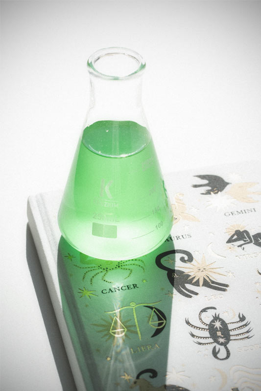 Un vase beige est posé sur une petite table en bois. Il contient de la pampa. À côté, une pile de livre ancien.